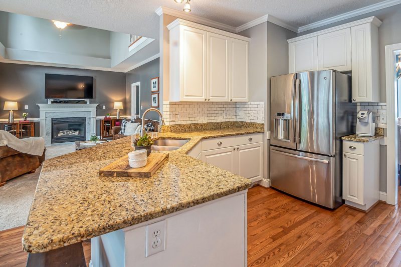 Luxurious open-concept kitchen with granite countertops and modern appliances adjacent to a cozy living room featuring a fireplace.