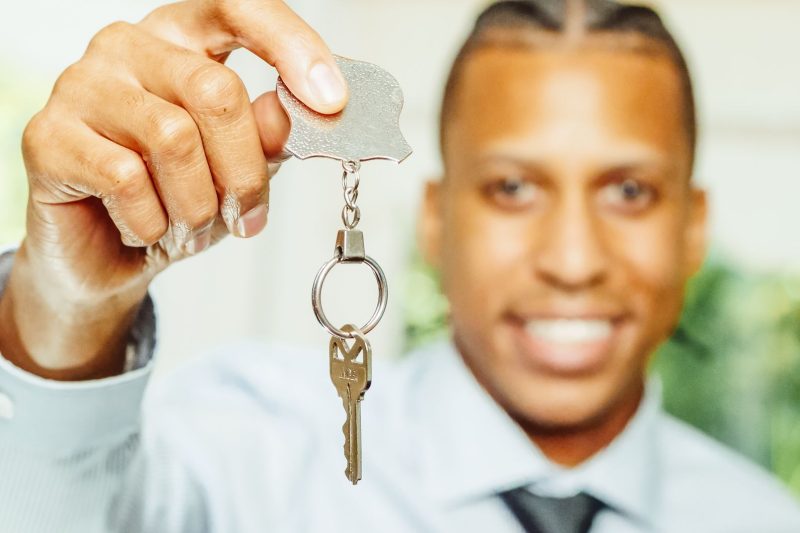 A smiling real estate agent holds out a house key, symbolizing home ownership.