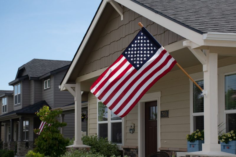 Vibrant American flag hanging outside a stylish suburban house in bright daylight.