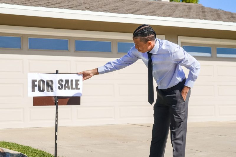 A real estate agent places a for sale sign outside a suburban house.