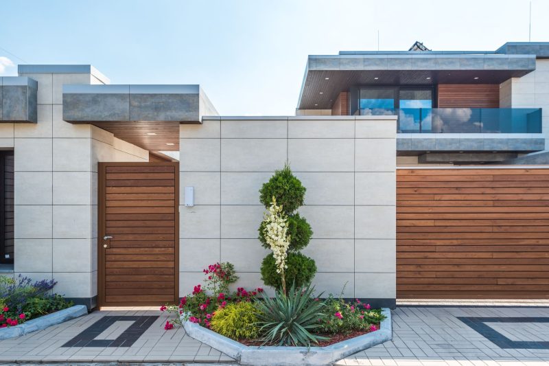 Contemporary house with a wooden facade, entrance gate, and a vibrant garden.