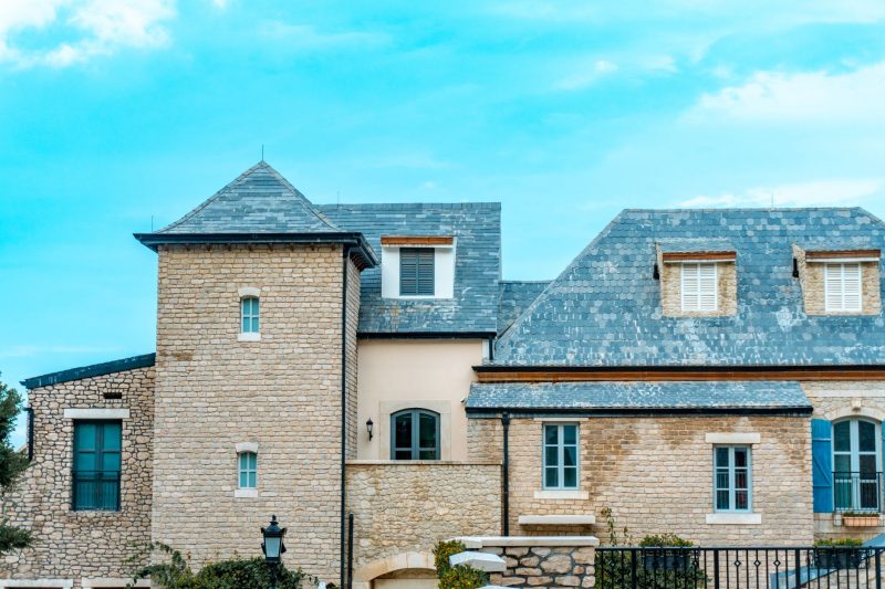 Picturesque stone house with a slate roof and blue shutters beneath a vibrant sky.
