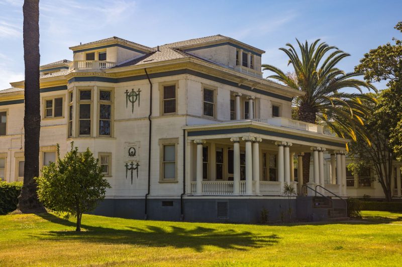 Elegant colonial mansion with classic columns surrounded by sunny landscaping.